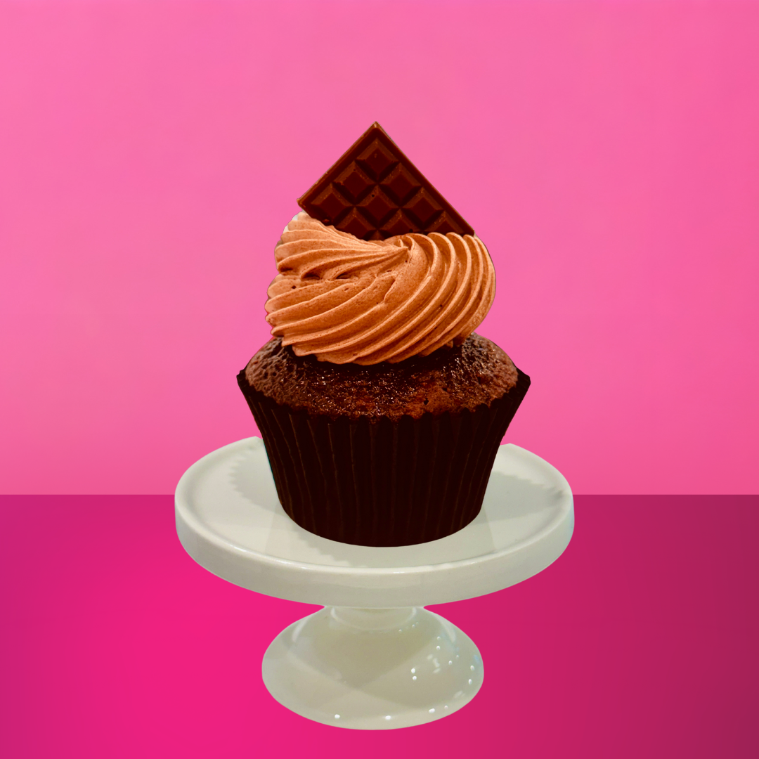 Chocolate cupcake with piped chocolate buttercream and a square of chocolate on top, displayed on a white stand with a pink backdrop
