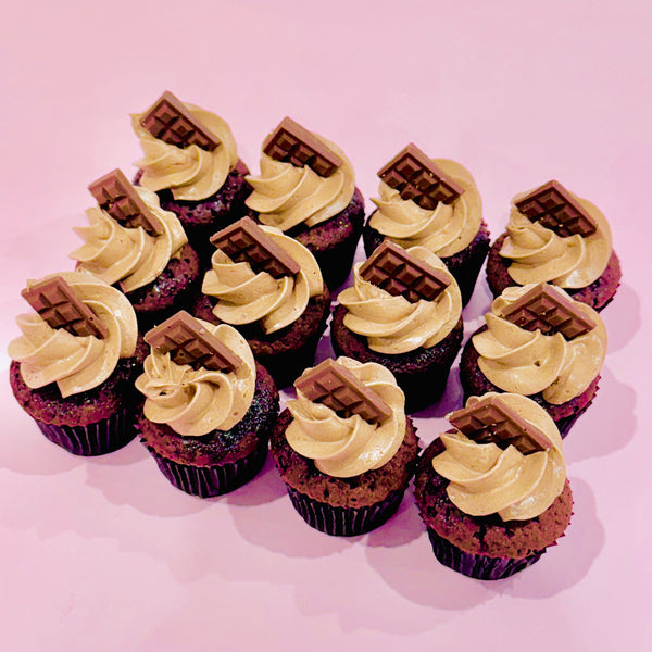 Mini chocolate cupcakes with piped chocolate buttercream and topped with a small milk chocolate block, arranged on a pink background.