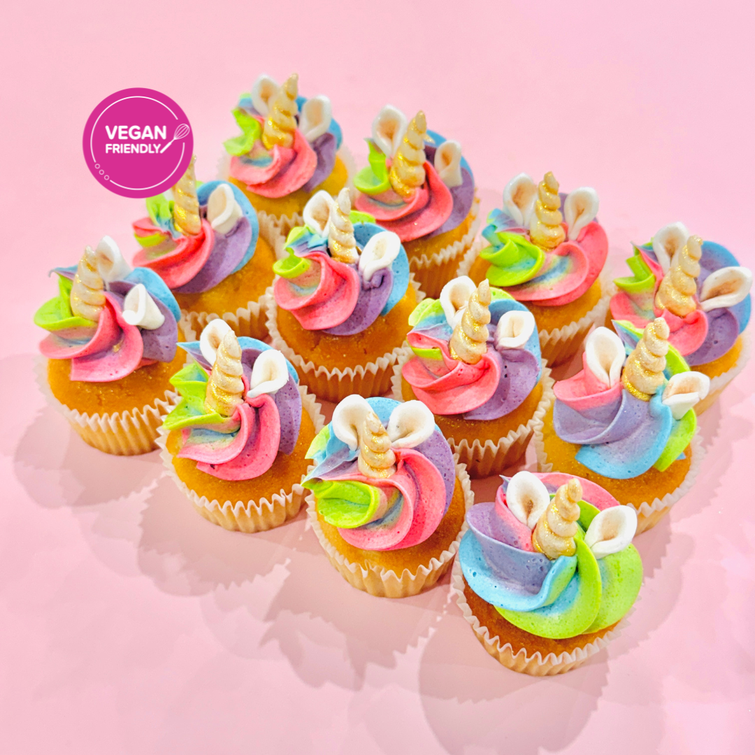 Mini cupcakes topped with rainbow swirls of pastel buttercream in pink, blue, green, and purple, finished with gold pearls and glitter on a pink background.