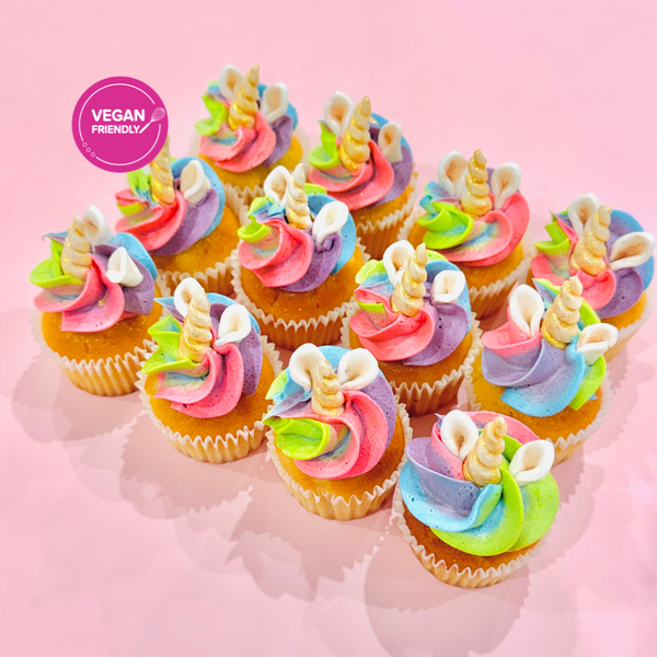 Mini cupcakes topped with rainbow swirls of pastel buttercream in pink, blue, green, and purple, finished with gold pearls and glitter on a pink background.
