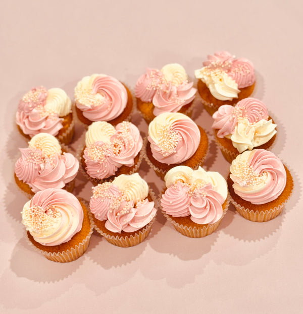 Pink and ivory baby shower cupcakes with multi-piped buttercream swirls, rosettes, and white pearl sprinkles on a pink background – perfect for a baby girl celebration.