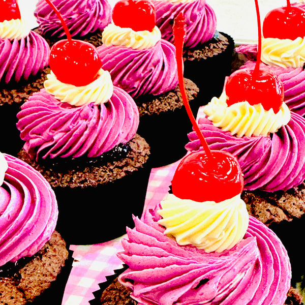 Chocolate cupcakes with pink frosting and red cherries on a checkered cloth.