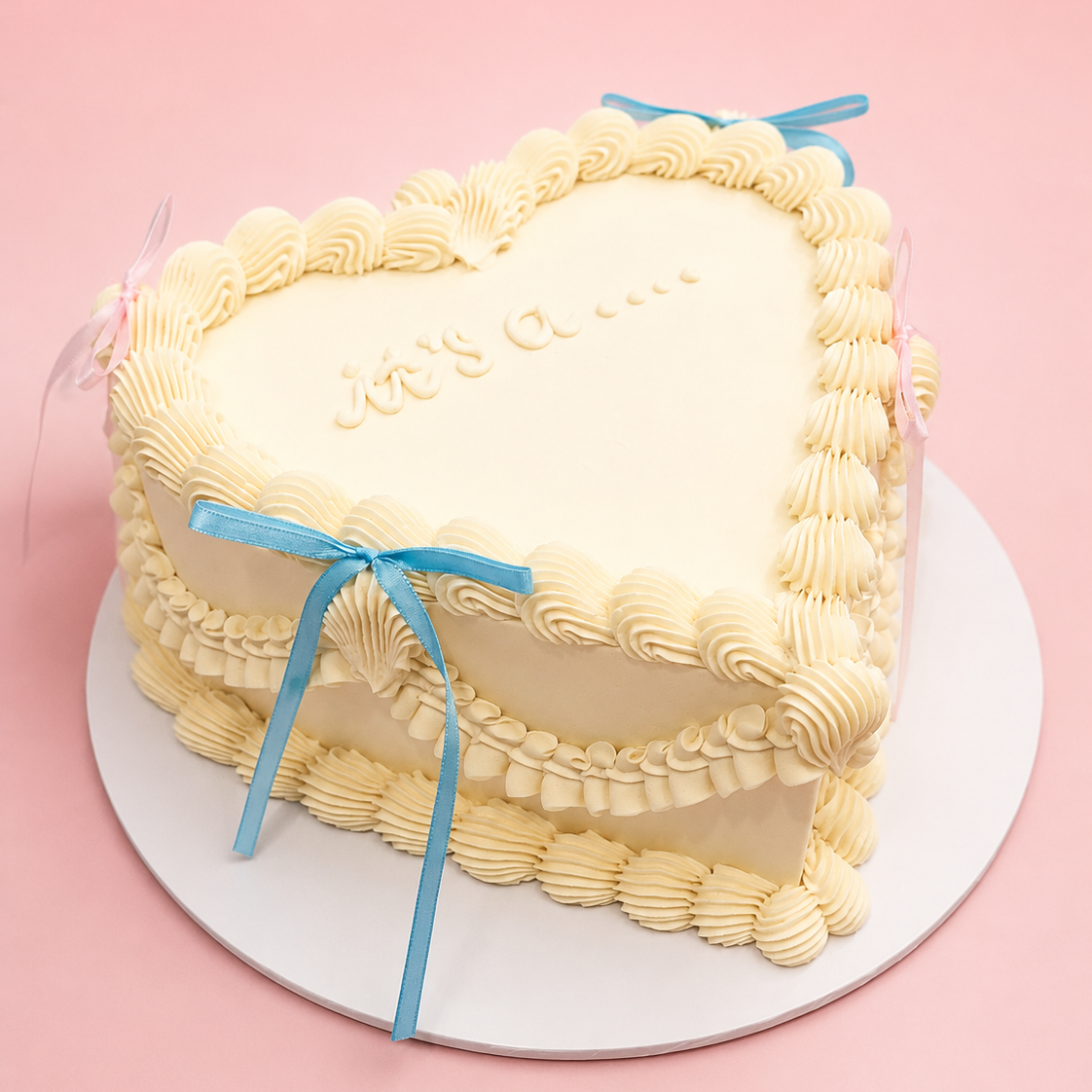 Heart-shaped cake with white frosting and blue ribbons on a pink background